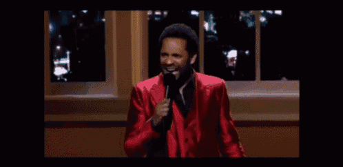 a man in a red suit is standing in front of a microphone and giving a speech .