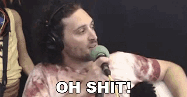 a man wearing headphones is sitting in front of a microphone and saying `` oh shit '' .