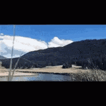 a lake surrounded by mountains and grass with a blue sky in the background
