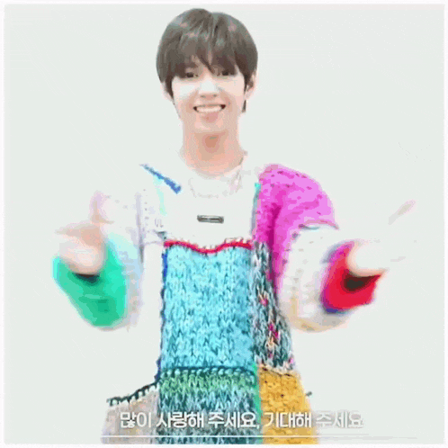 a young man is wearing a colorful sweater and making a heart shape with his hands .