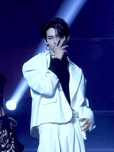 a man in a white suit is holding a microphone and covering his face