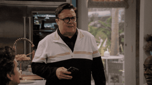 a man wearing glasses and a black and white jacket holds a cell phone