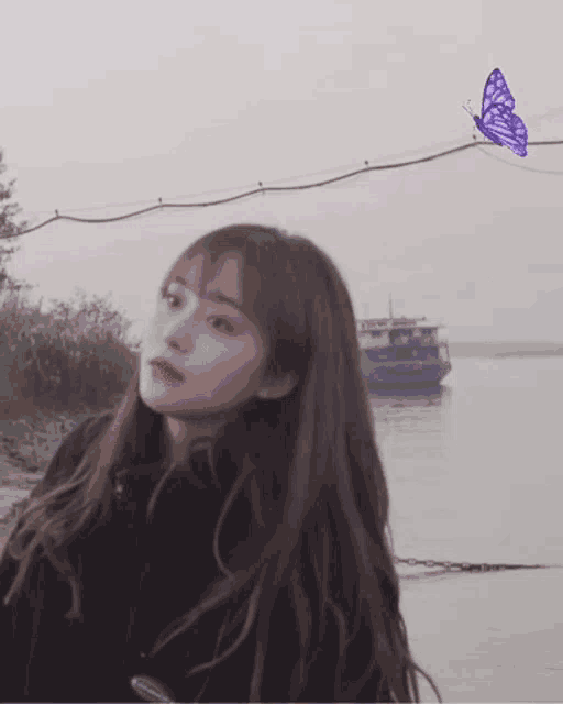 a girl is standing in front of a body of water with a purple butterfly flying over her head