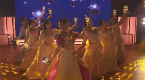 a group of women in long dresses are dancing on a stage holding candles .