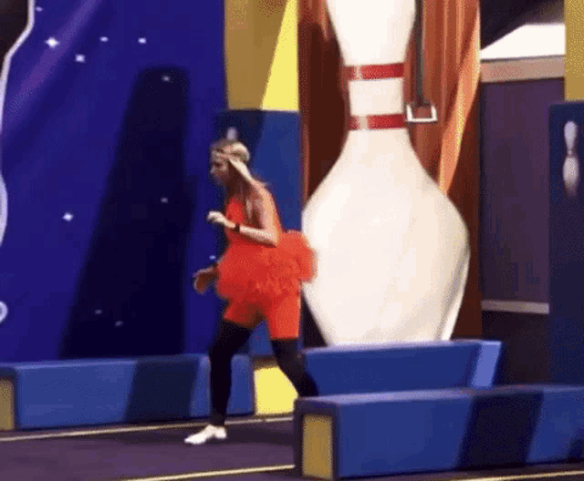 a woman in a red dress is standing next to a bowling pin