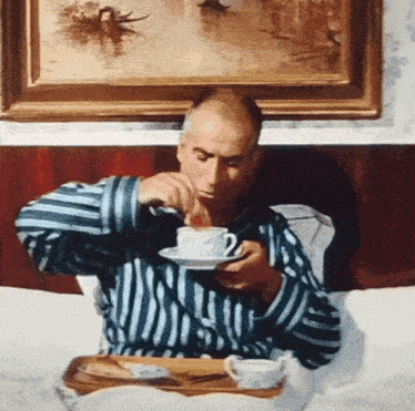 a man in a blue and white striped shirt is drinking from a white cup