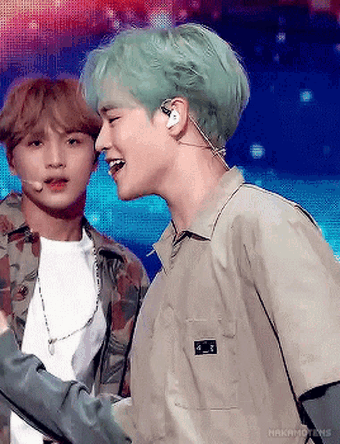 two young men are standing next to each other on a stage . one of the men has green hair and the other has brown hair .