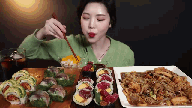 a woman is sitting at a table eating sushi and noodles