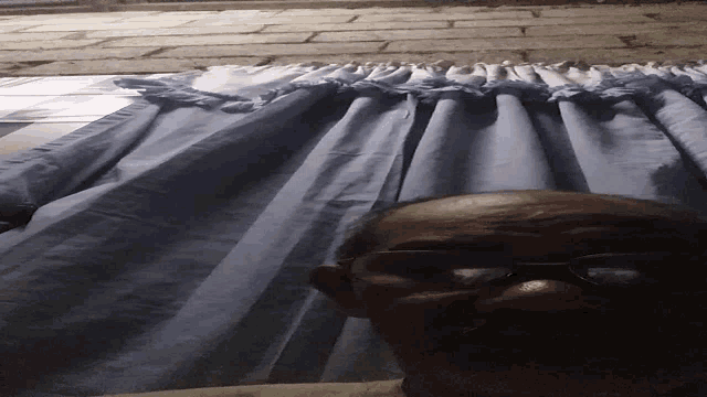 a man laying on a bed with his eyes closed and a blue curtain behind him
