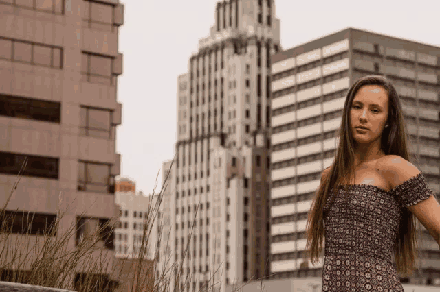 a woman stands in front of tall buildings in a city