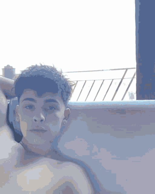a shirtless young man laying in a bathtub looking at the camera