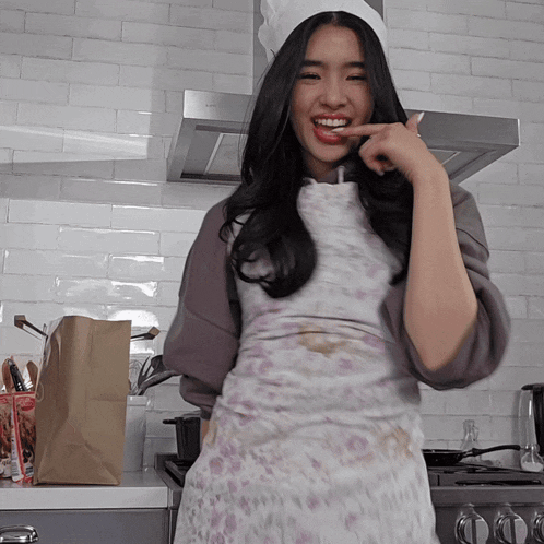 a woman wearing an apron and a chef 's hat smiles in a kitchen