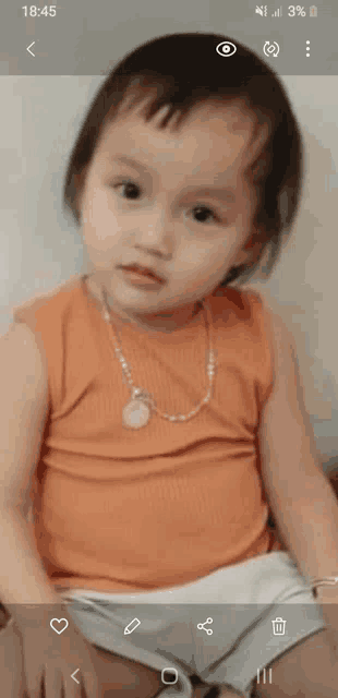 a little girl wearing an orange tank top and a necklace looks at the camera