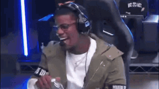a man wearing headphones and glasses is sitting in a chair and laughing .