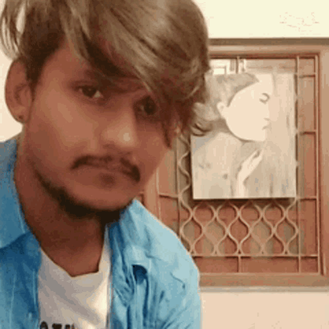 a man in a blue shirt is looking at the camera with a picture of a woman in the background