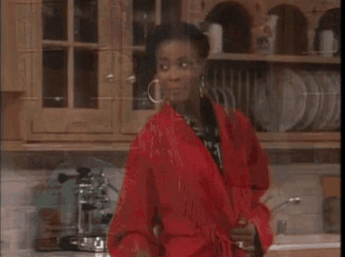 a woman in a red robe is walking in a kitchen .