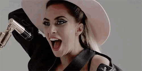lady gaga is wearing a pink hat and holding a microphone with her tongue out .