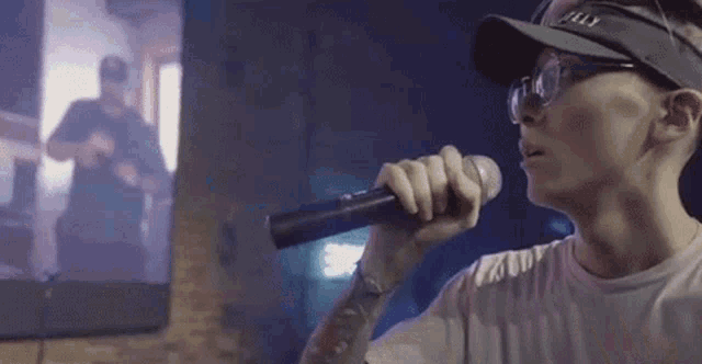 a man is singing into a microphone while wearing a hat and glasses .
