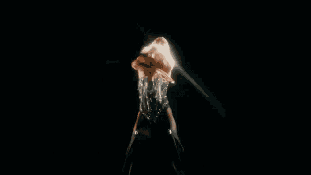 a woman with long blonde hair is dancing in a dark room with a black background .