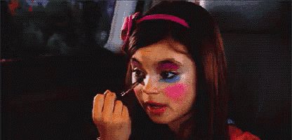 a little girl is applying makeup to her face while wearing a pink headband