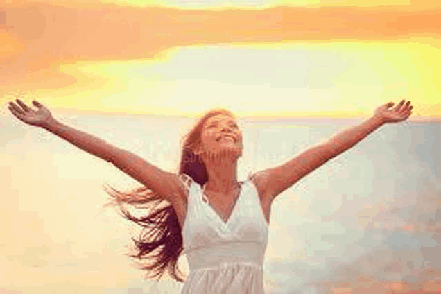 a woman in a white dress is standing on the beach with her arms outstretched at sunset .