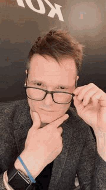 a man wearing glasses and an apple watch is holding his hand to his chin .