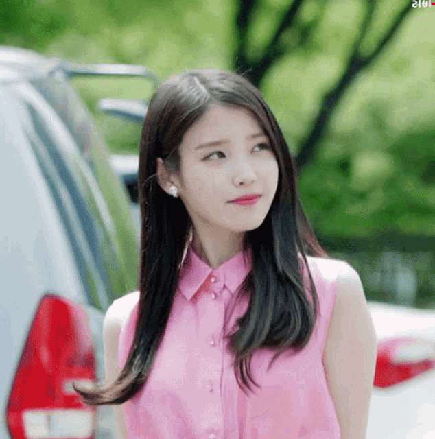 a woman wearing a pink shirt is standing in front of a car