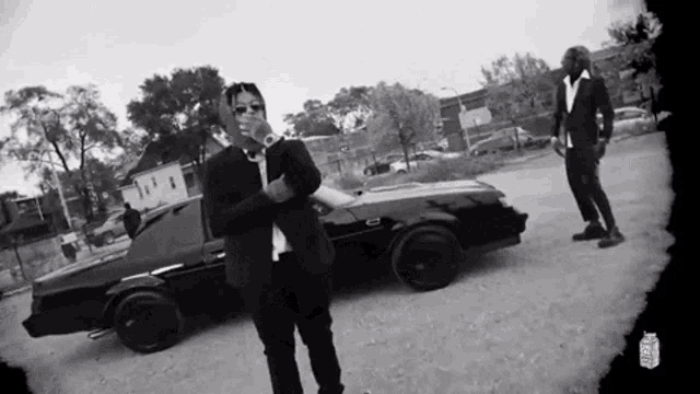 a man in a suit is standing in front of a black car
