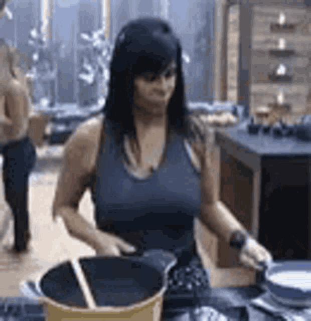 a woman is cooking in a kitchen while holding a pot and a spatula .