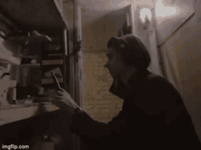 a man is looking into a fridge with a cell phone in his hand