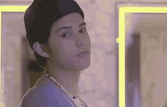a young man wearing a hat and a pearl necklace looks at the camera