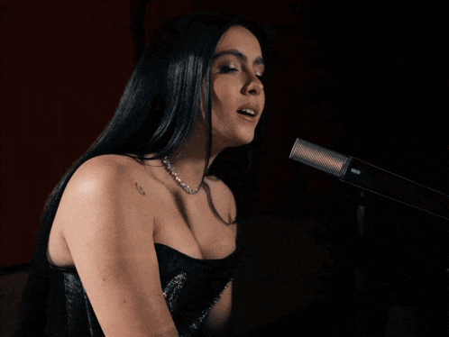 a woman singing into a microphone with a tattoo on her arm that says ' g '