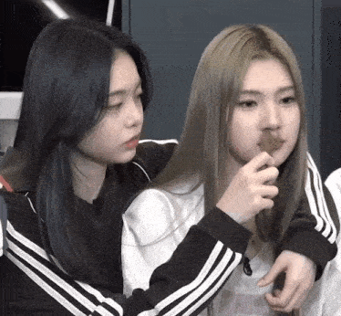 two girls are standing next to each other and one is holding something in her mouth .