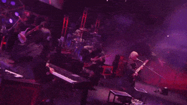 a group of people playing guitars in a dark room with purple lights behind them