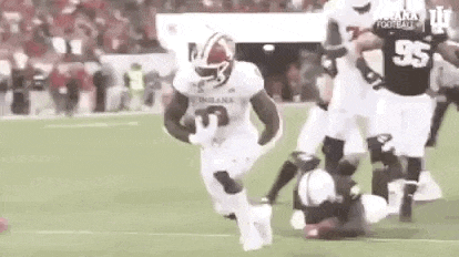 a football player is running with the ball on a field while a player is laying on the ground .