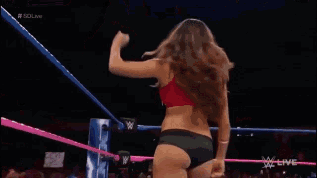 a woman in a red top is standing in a wrestling ring next to a referee who is wearing a striped shirt