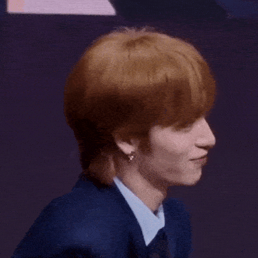 a close up of a person 's face with red hair wearing a blue suit and tie .