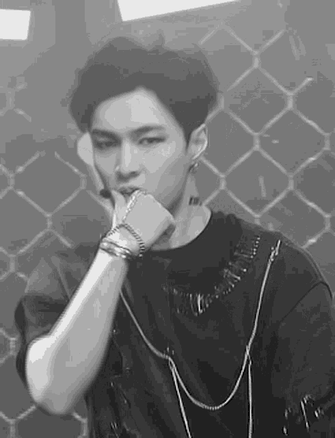 a black and white photo of a young man wearing a black shirt and bracelets .