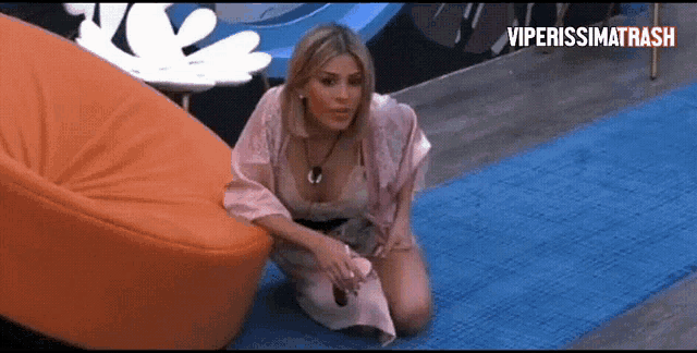 a woman in a pink robe is kneeling on a blue rug next to an orange chair