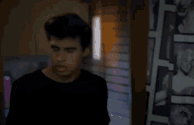 a young man in a black shirt is looking at himself in the mirror