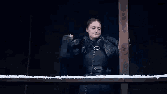 a woman in a black coat is standing next to a wooden railing in a dark room .