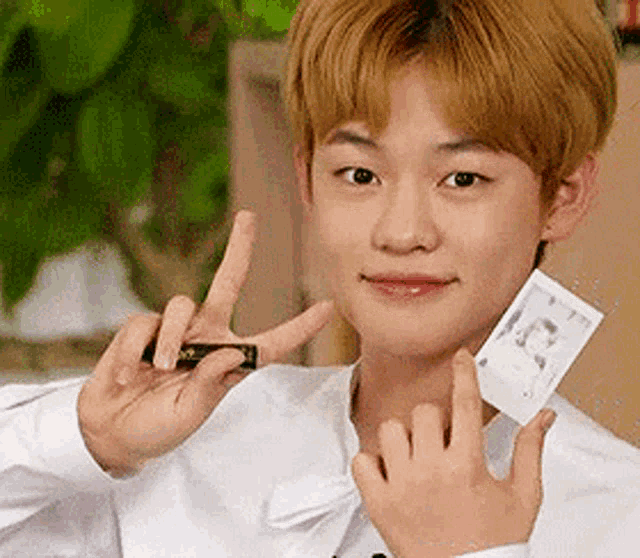 a young man in a white shirt is holding a polaroid picture and making a peace sign .