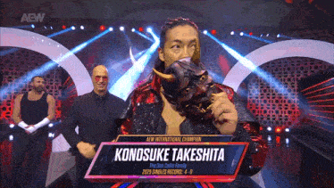 a wrestler named konosuke takeshita holds a demon mask on a stage