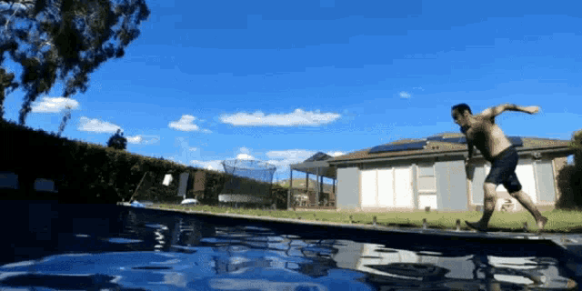 a man jumps into a swimming pool with a house in the background