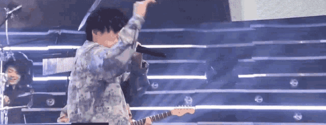 a man is playing a guitar on a stage while singing into a microphone .