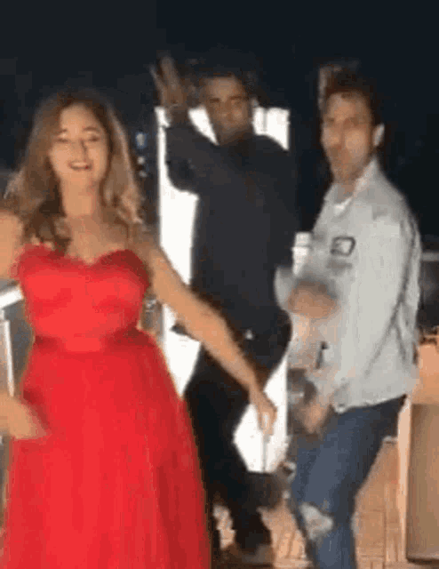 a woman in a red dress is dancing with two men in a room .