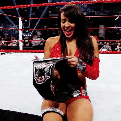 a woman in a wrestling ring is holding a belt that says ' world heavyweight champion ' on it