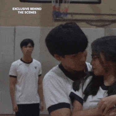 a boy and a girl are hugging in a gym with the words exclusive behind the scenes written above them