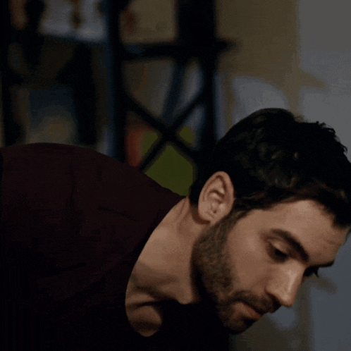 a man with a beard wearing a burgundy shirt looks down