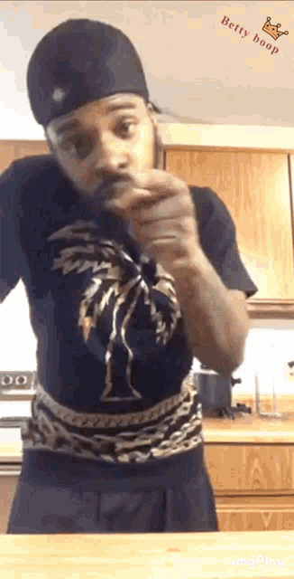 a man wearing a black shirt with a palm tree on it stands in a kitchen